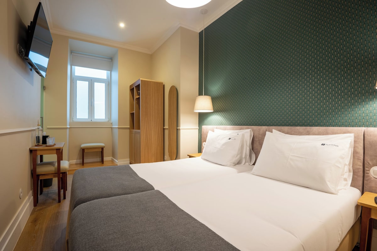 Une chambre d’hôtel comprenant un lit, un téléviseur fixé au mur, une fenêtre, un bureau avec une chaise et une armoire.