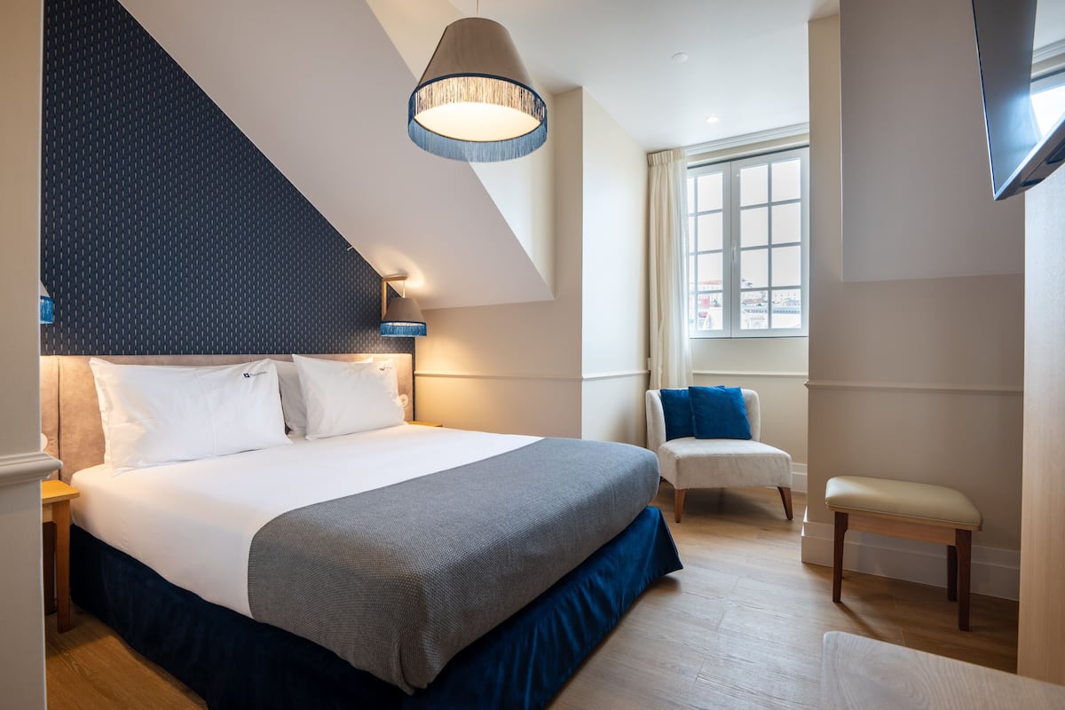 Une chambre moderne avec un grand lit, une chaise, un banc et une fenêtre avec des rideaux.