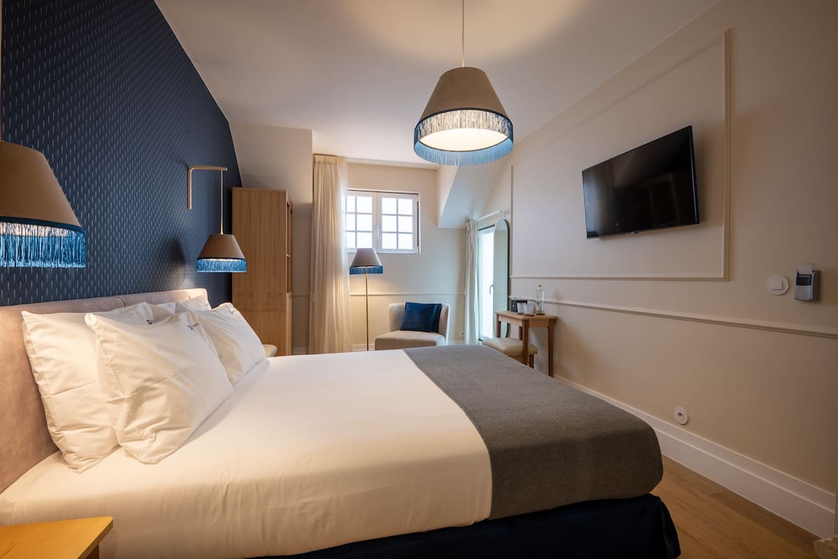 Une chambre d’hôtel moderne avec un grand lit, un téléviseur fixé au mur et une fenêtre avec des rideaux.