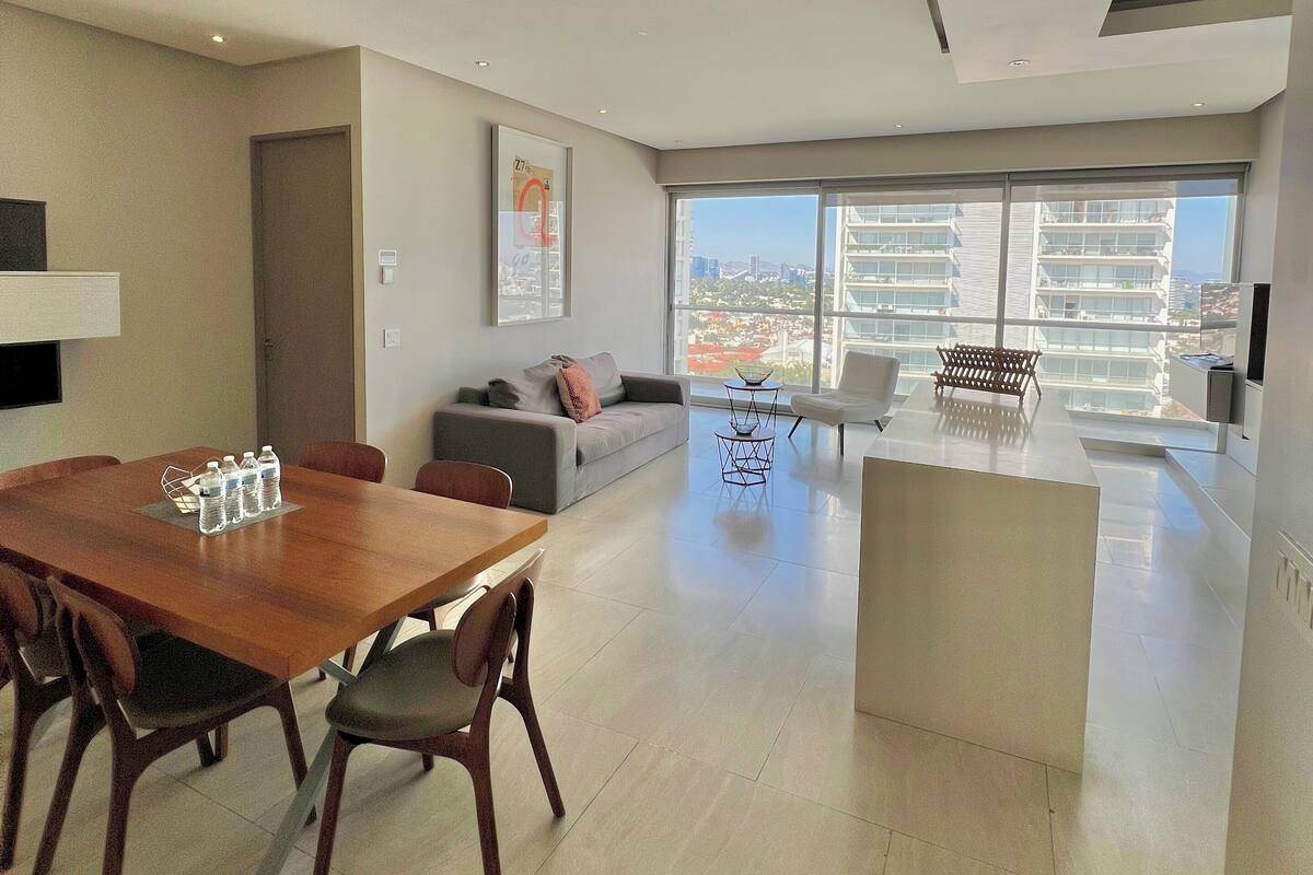 Amplia sala de estar con mesa de comedor, sofás y un gran ventanal con vistas a la ciudad.