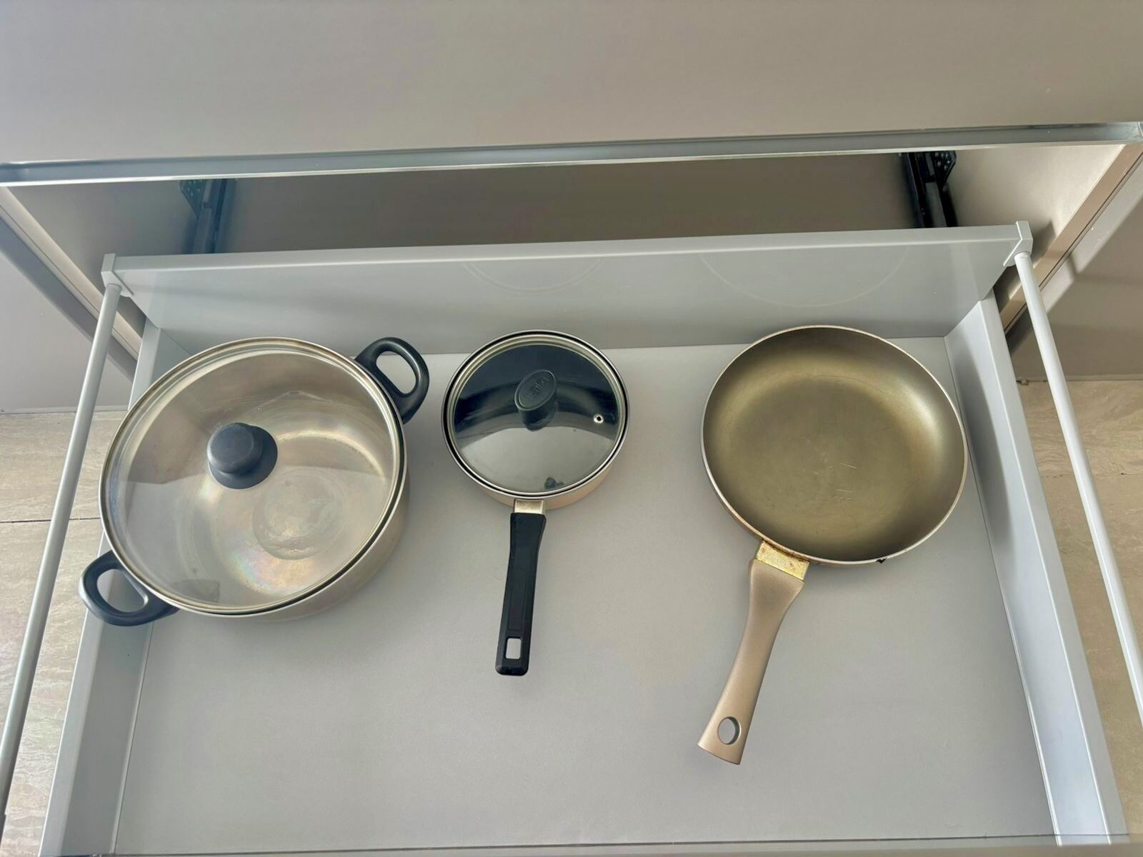 Un tiroir de cuisine contenant trois casseroles et trois poêles.