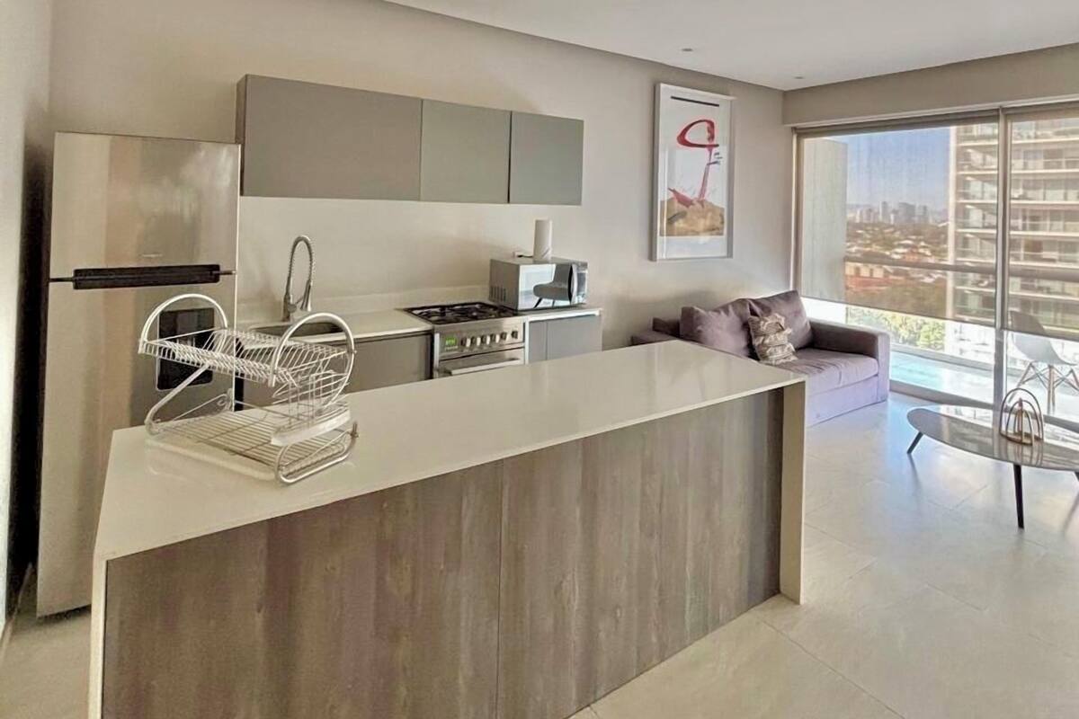 Una cocina moderna con una isla central, electrodomésticos de acero inoxidable y un amplio ventanal con vistas a la ciudad.