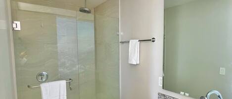 A modern bathroom with a glass-enclosed shower, a white toilet, a granite countertop, and a large mirror.