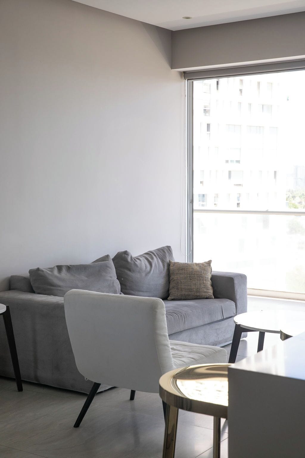 Un salon moderne avec un canapé gris, un fauteuil blanc et une petite table ronde.