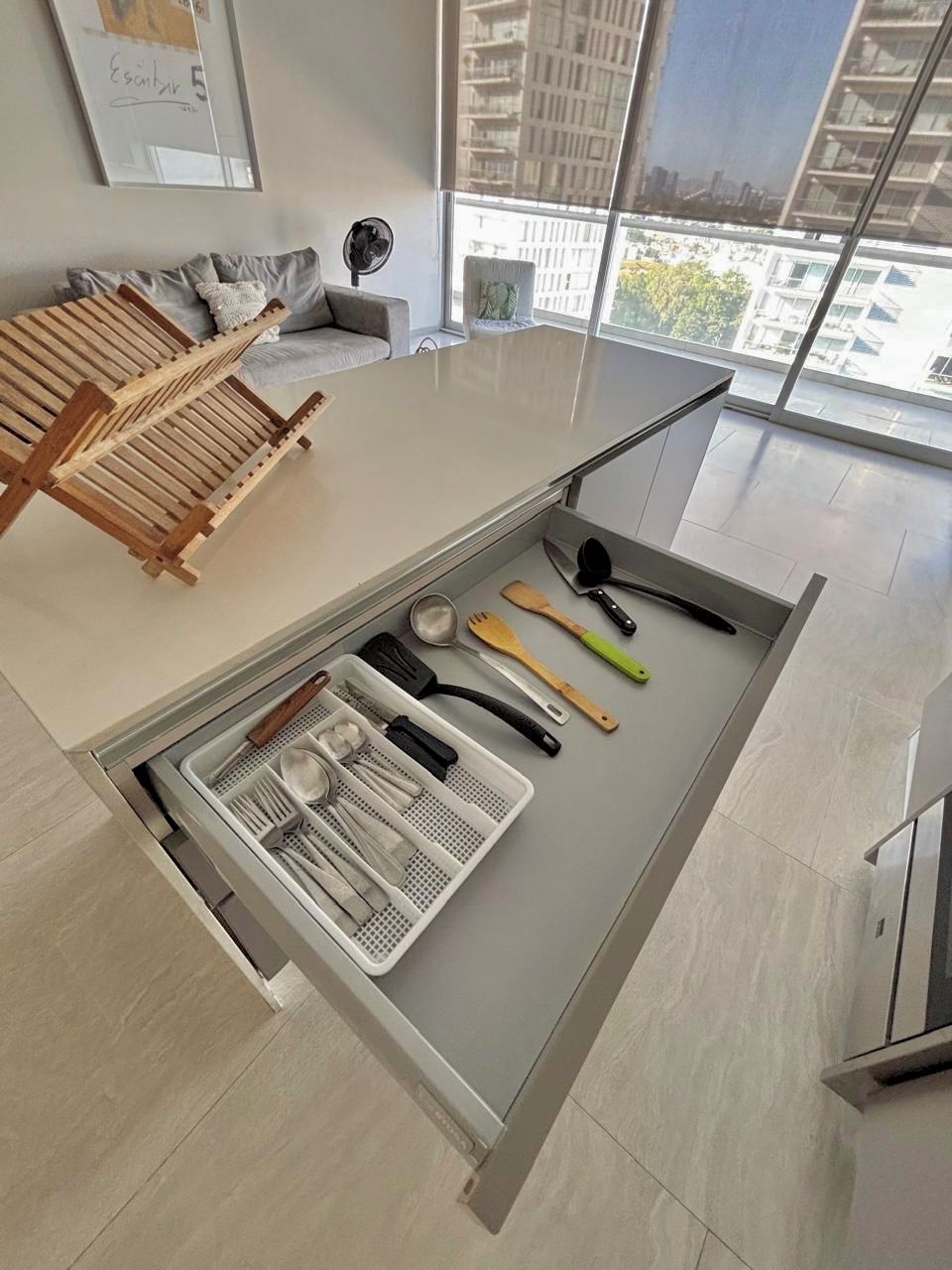 A modern kitchen with a built-in drawer containing kitchen utensils and a wooden drying rack.