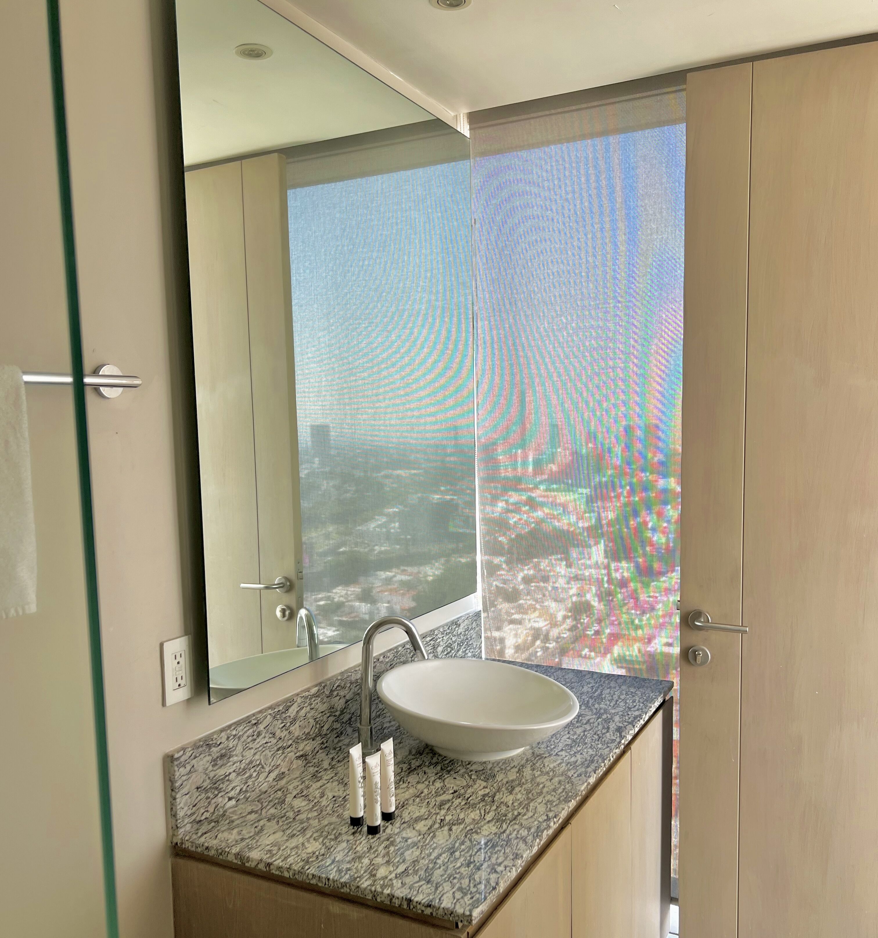 Une salle de bain avec un grand miroir, un lavabo et une vue sur le paysage urbain par une fenêtre.