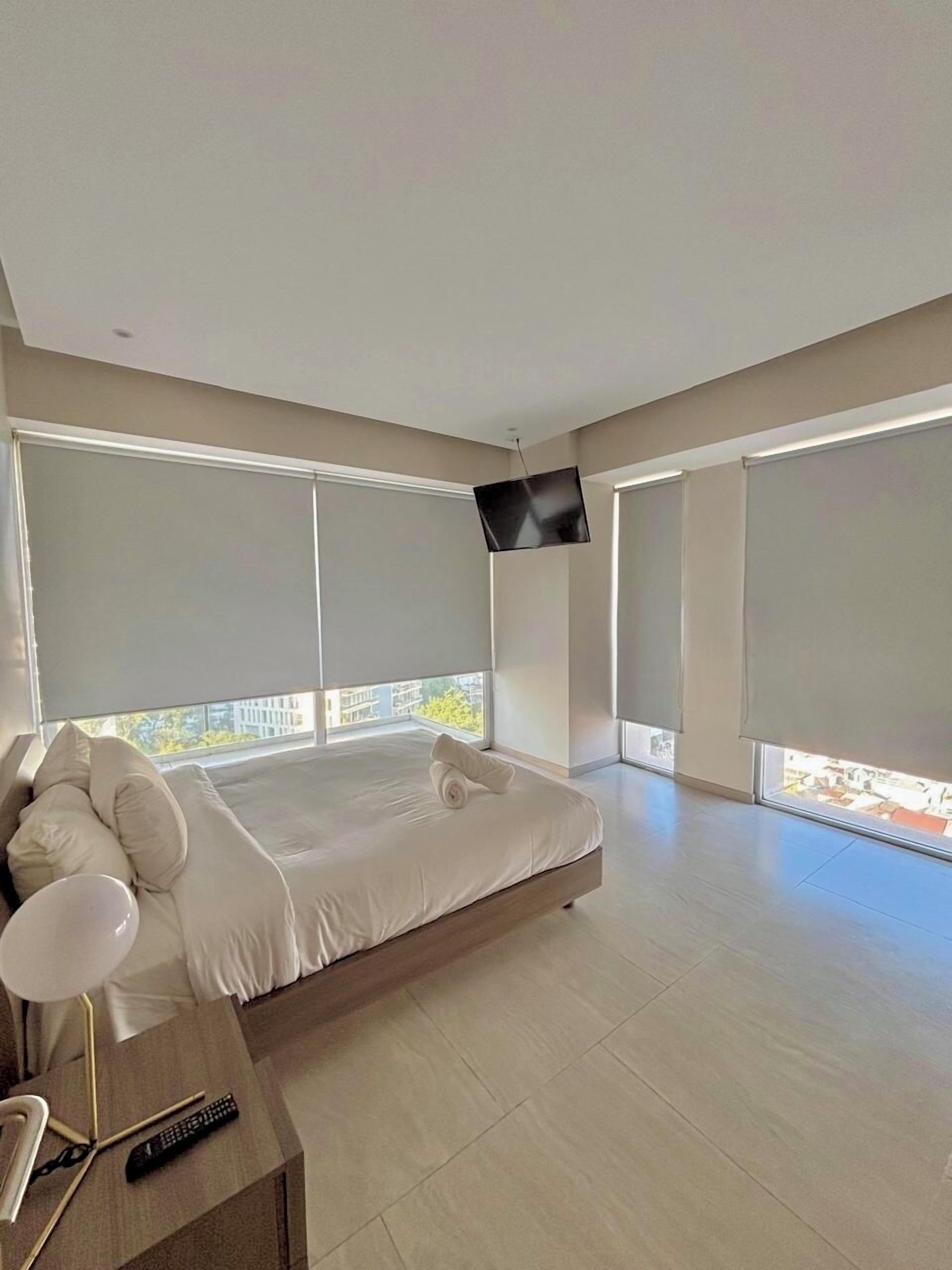 A modern bedroom with a large bed, a TV mounted on the wall, and a balcony with a view.