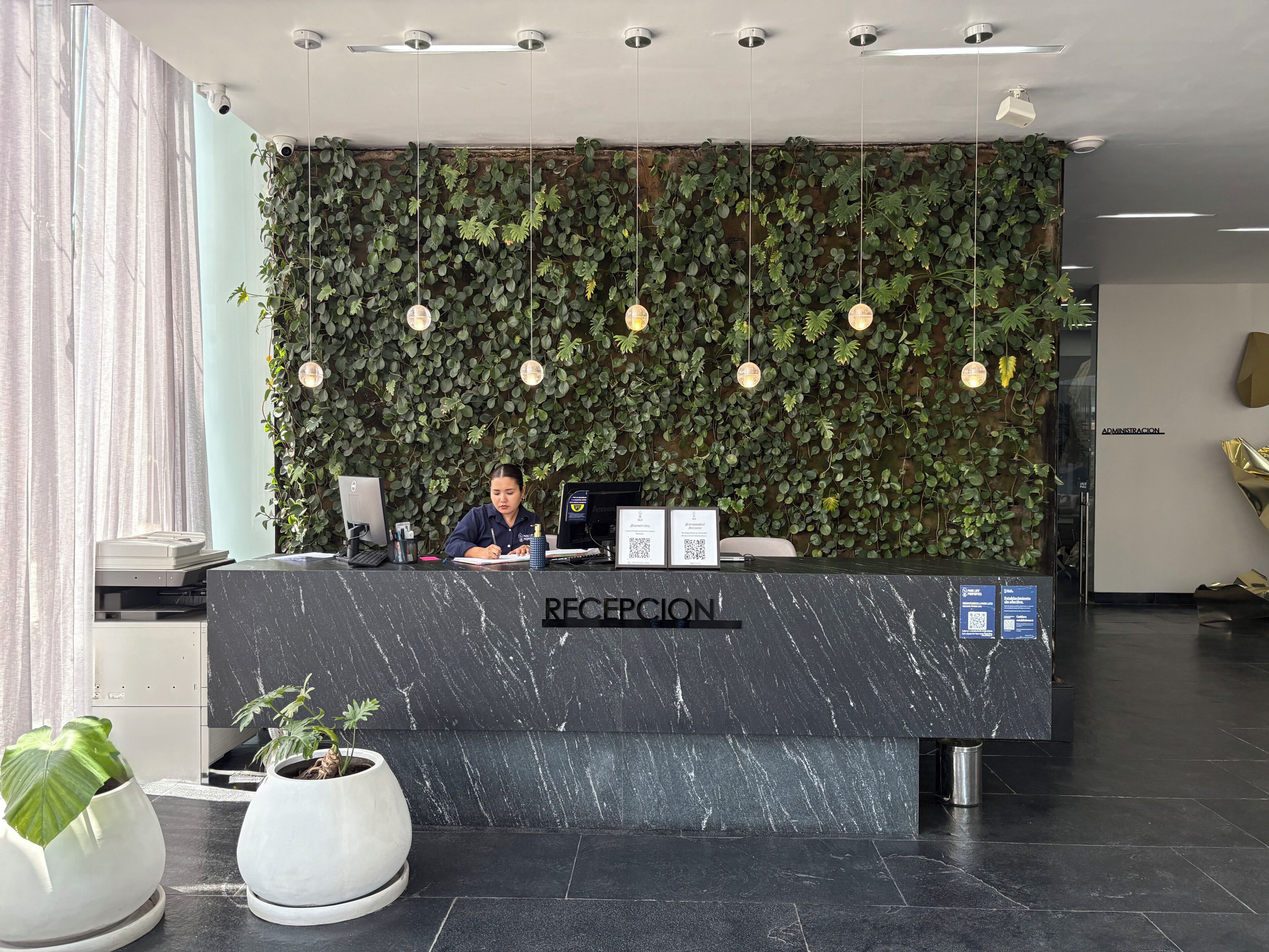 Un comptoir d’accueil avec un plateau en marbre, un mur recouvert de verdure et des luminaires suspendus.