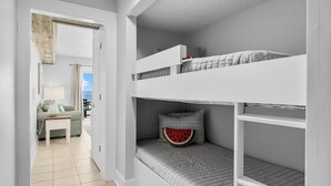 Une chambre avec un lit superposé donnant sur l’extérieur, une petite table avec une lampe et un canapé vert.