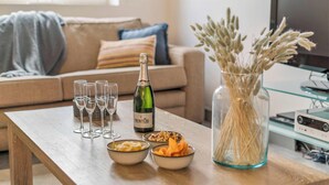 En stue med et træbord, champagne, glas, skåle med snacks og en vase med tørrede planter.