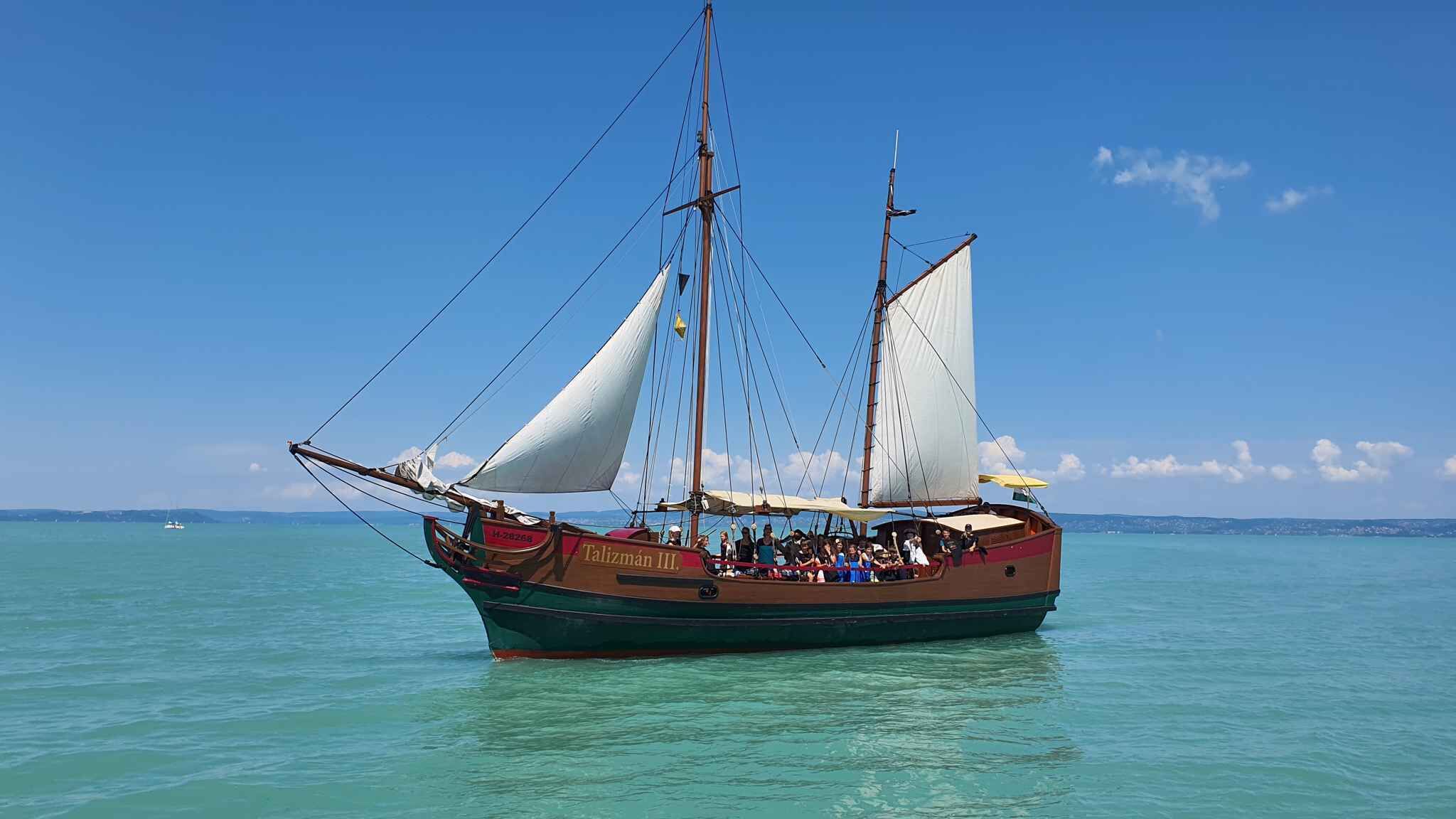 Un voilier traditionnel doté de plusieurs voiles, transportant des passagers, sous un ciel bleu azur.