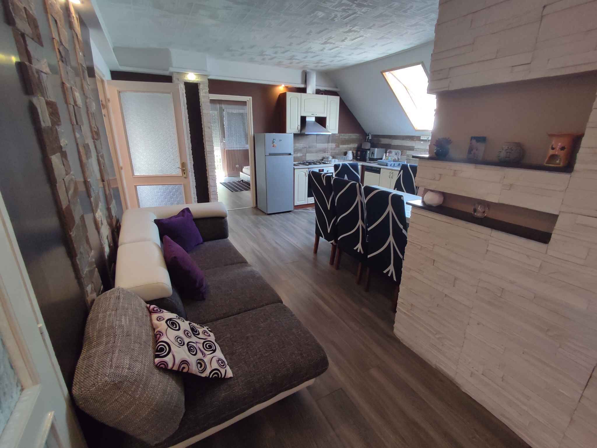 A compact living space with a sofa, a dining table with chairs, a kitchen area, and a small window.