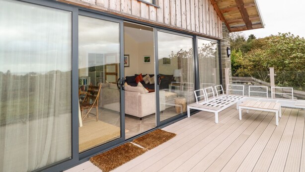 A modern house with large glass windows, a wooden deck, and a cozy interior with a sofa and a coffee table. - The Lodge (Stranraer)