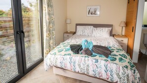 A bedroom with a bed, a nightstand, a lamp, a picture on the wall, and a sliding glass door to the outside. - The Lodge (Stranraer)