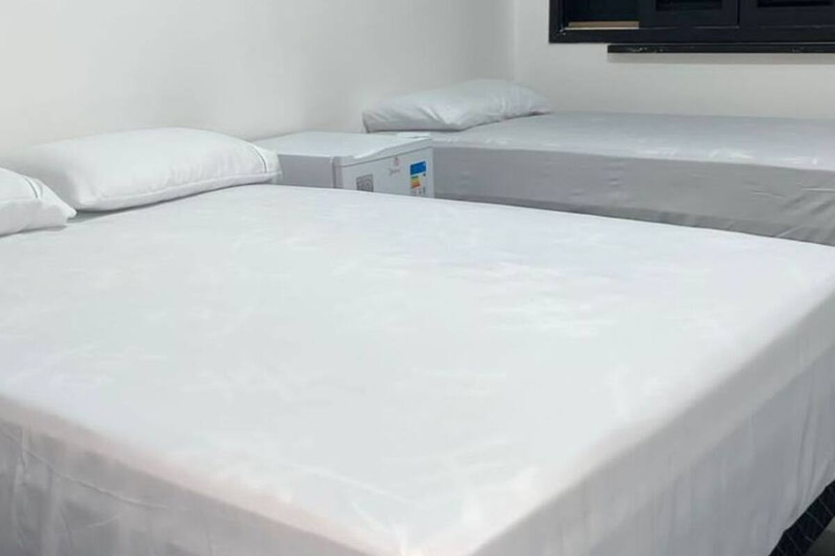 Une chambre d’hôtel avec deux lits, chacun étant équipé de draps et d’oreillers blancs. On y trouve une petite table de chevet avec une lampe et une prise de courant.