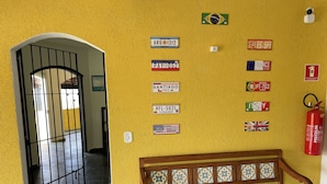 A hallway with a yellow wall, a wooden bench, and various international license plates. - Suítes Temporada Favorita (Peruíbe)
