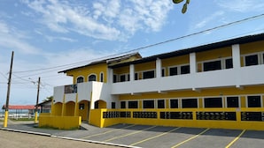 A yellow and white building with a parking lot in front. - Suítes Temporada Favorita (Peruíbe)