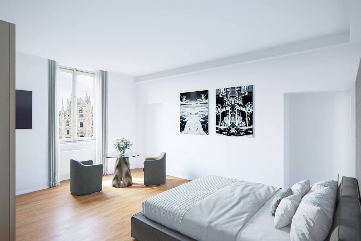 Habitación de hotel moderna con una cama grande, una mesita redonda pequeña, dos sillones y vistas a un edificio histórico a través de un amplio ventanal.