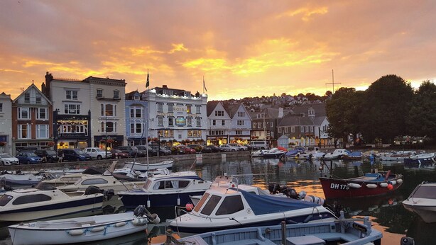 A marina with several boats docked, surrounded by buildings including a hotel with a sign reading "CASTLE ROYAL HOTEL". - Dancing Beggars (Dartmouth)