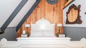A bedroom with a white ornate bed, two bedside tables with lamps, a wooden wall panel, and a large mirror. - Dancing Beggars (Dartmouth)