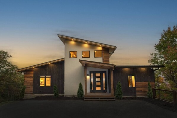 A modern two-story house with a prominent entrance, multiple windows, and a well-lit facade. - Best View in Smokies Modern Lux Pool Games Hot Tub (Sevierville)