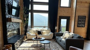 Ein gemütliches Wohnzimmer mit Kamin aus Stein, großen Fenstern und Bergblick.