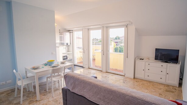 A modern apartment with a dining area, a sofa, a TV, and a balcony with a city view.