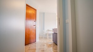 A hallway leading to a dining area with a wooden door, white chairs, and a table.