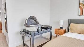 A room with a bed, a nightstand with a lamp, a baby crib, and a wall-mounted artwork.