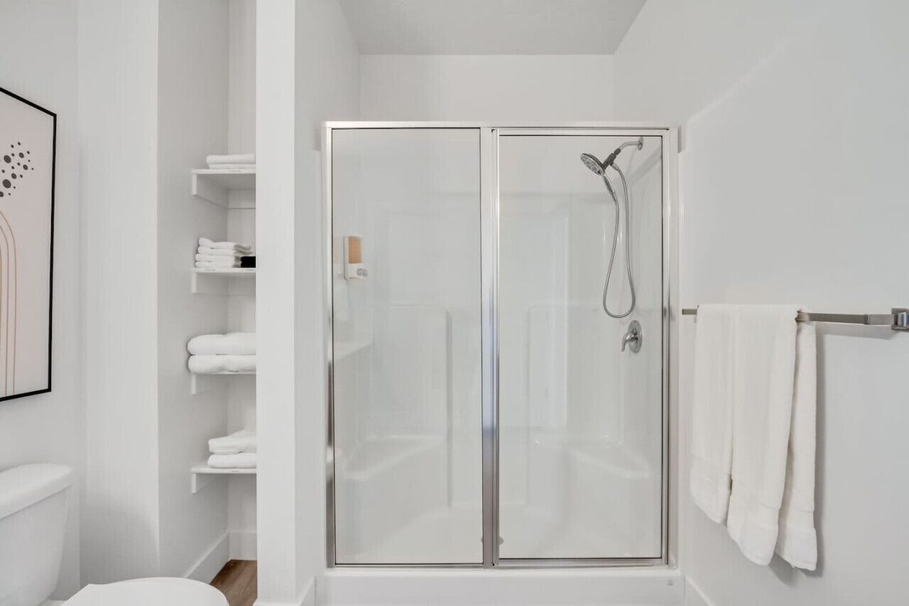 Un baño moderno con ducha de vidrio, repisas blancas con toallas y un inodoro.