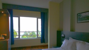 Habitación de hotel con una cama grande, una mesita de noche, una ventana con cortinas y un cuadro en la pared.