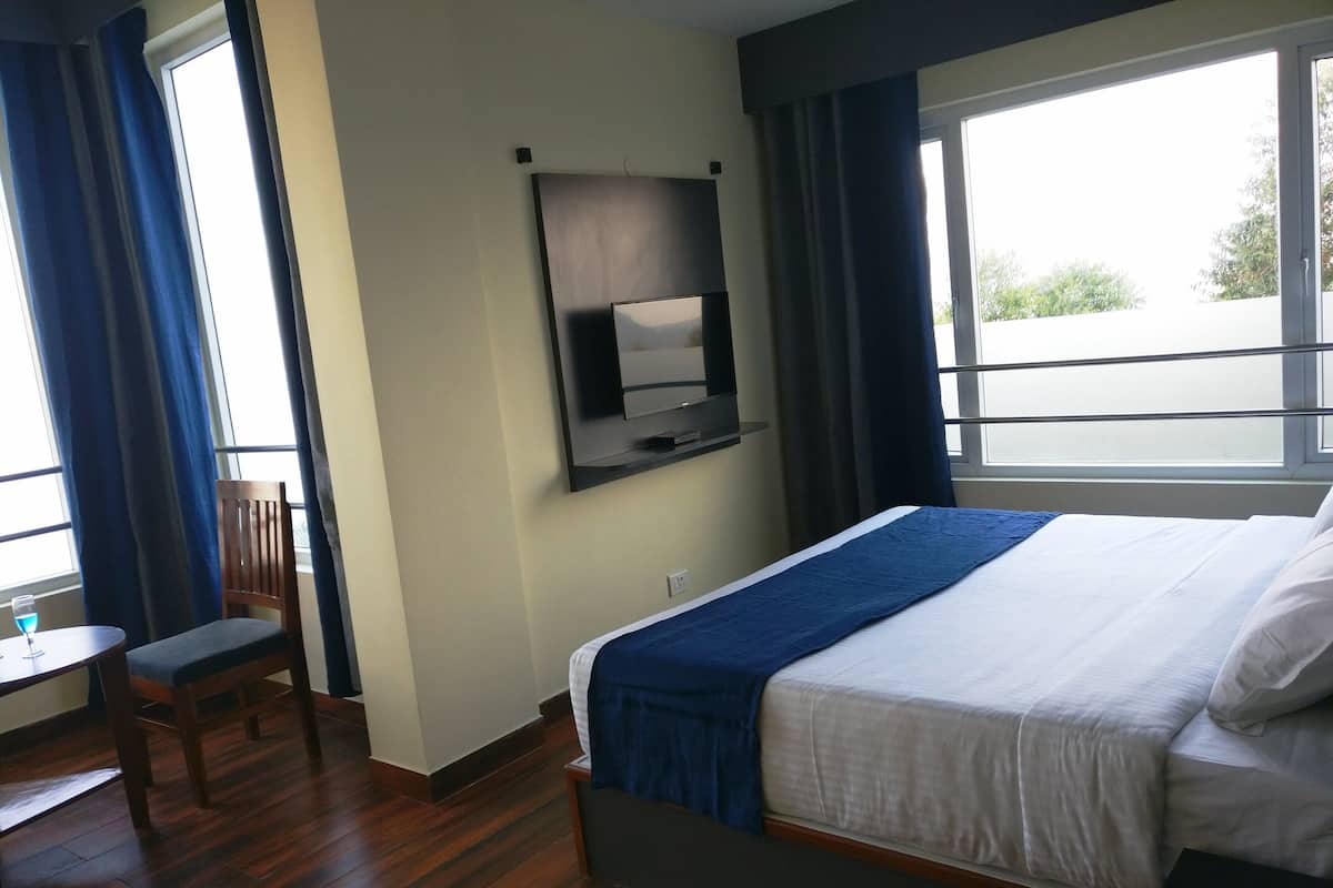Habitación de hotel con cama, televisor montado en la pared, escritorio con silla y ventana con cortinas.