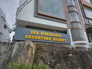 Ein Schild für 'SKR SIVABHAGYA ADVENTURE RESORT' mit einer Steinmauer und Pflanzen im Vordergrund.