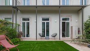 Un edificio moderno con techo plano, ventanas grandes y un pequeño patio con césped y zona de estar.
