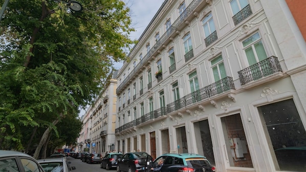 Une rangée de bâtiments de style européen classique, à l’architecture uniforme, avec des voitures garées le long de la rue et des arbres bordant le trottoir.