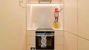 Une cuisine compacte dotée d’un four encastré, d’un extincteur fixé au mur et d’un petit plan de travail sur lequel se trouvent une bouteille et des ustensiles.
