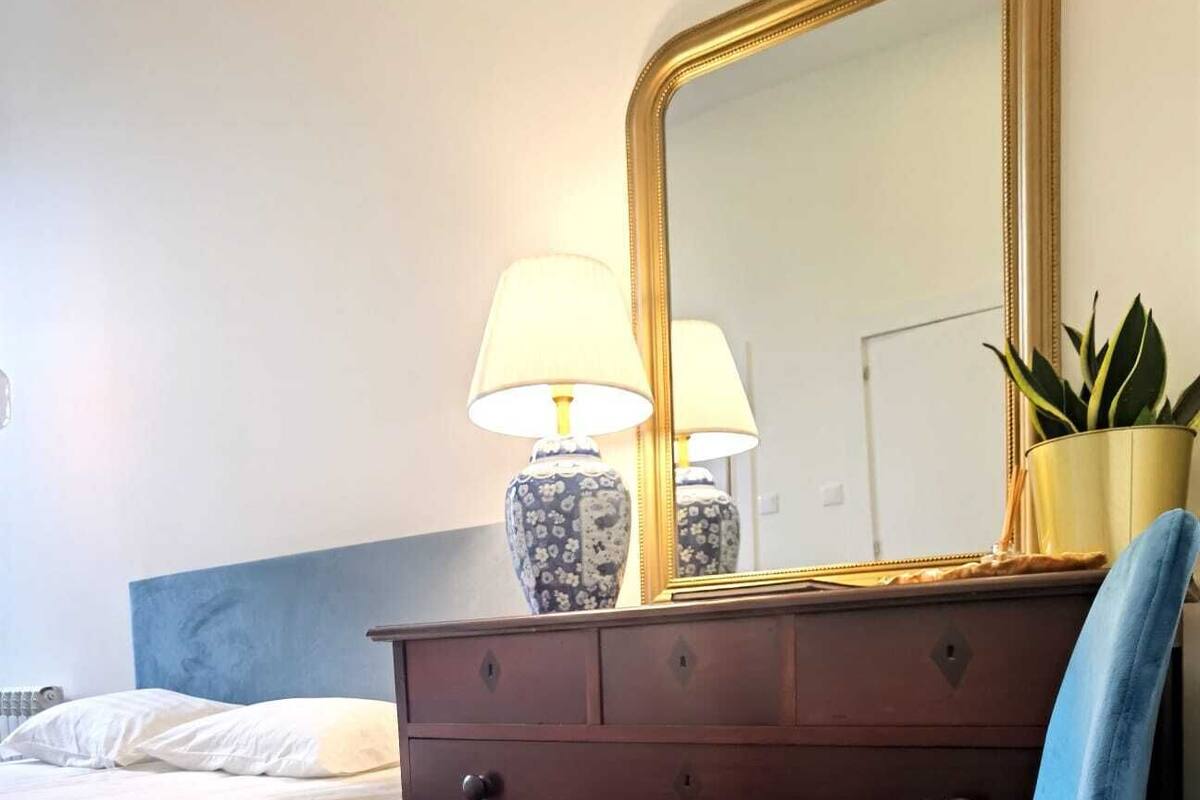 A bedroom with a bed, a dresser, a chair, a mirror, and a lamp.