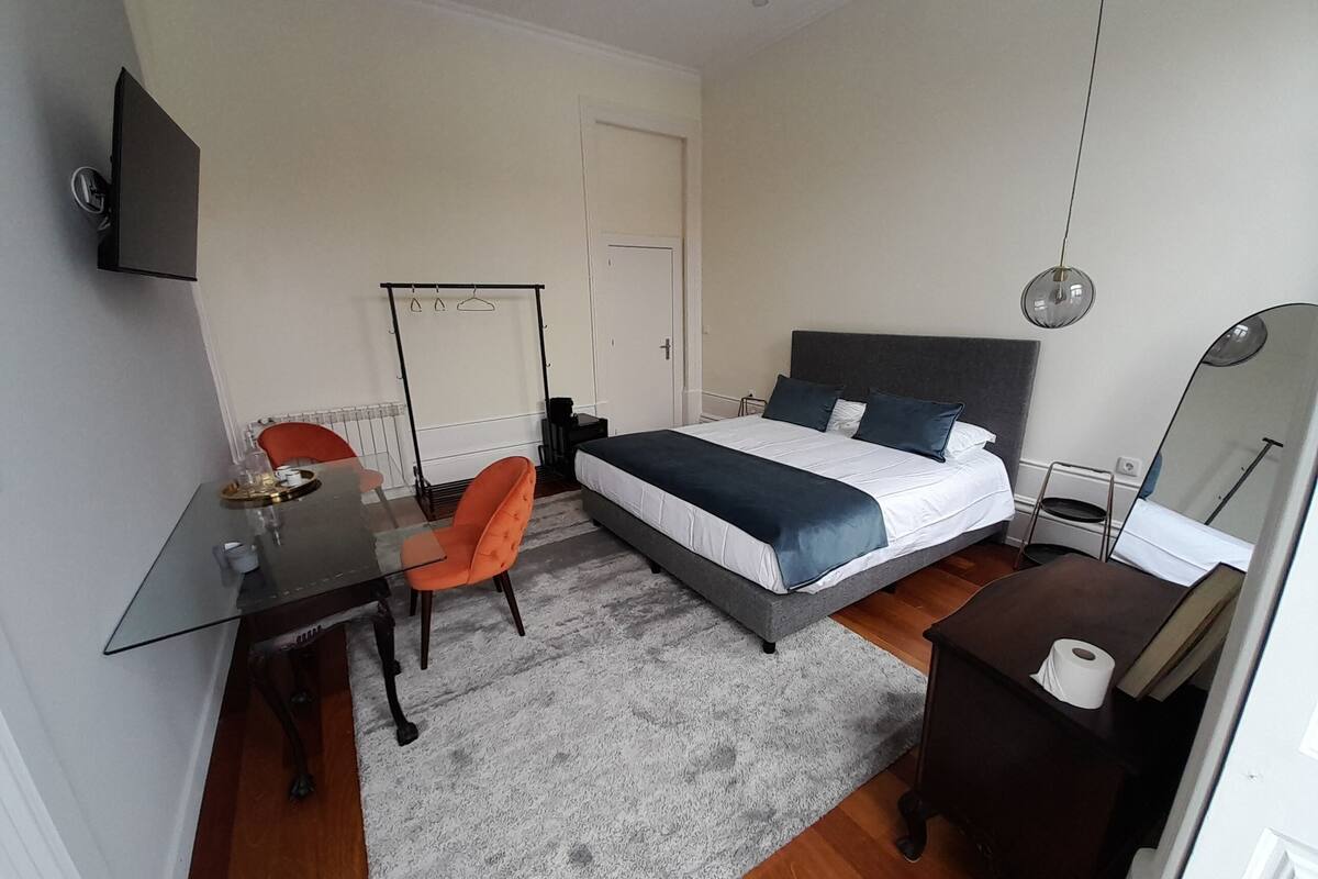 A bedroom with a bed, bedside table, chair, desk, and a mirror.