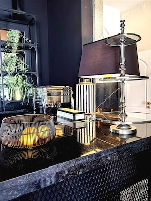 Una cocina moderna con encimera de mármol, un bol de metal con limones, un jarrón a rayas y una lámpara con pantalla oscura.