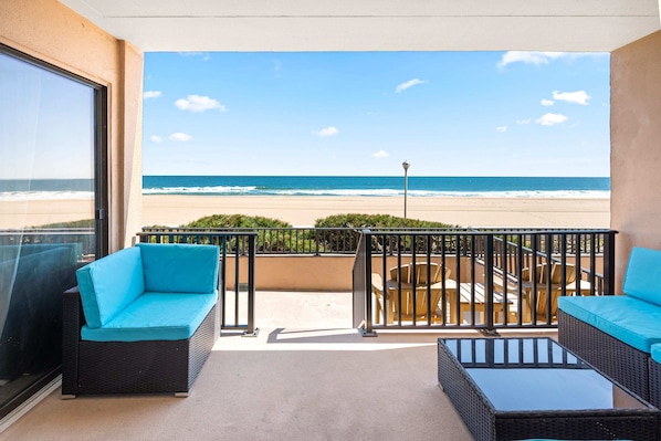 Un balcón con vista a la playa, mobiliario de mimbre y una mesa de vidrio.
