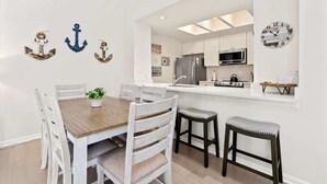A dining area with a wooden table, white chairs, and a small plant. There are three anchors on the wall. - 2 Blocks from the Beach: The Coquina Cottage (Jacksonville Beach)