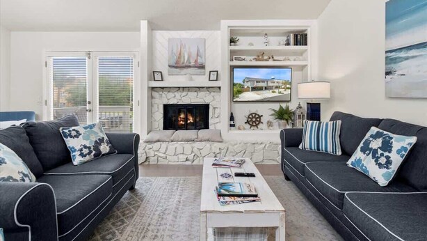 A living room with two dark sofas, a stone fireplace, a television, and a bookshelf. - 2 Blocks from the Beach: The Coquina Cottage (Jacksonville Beach)