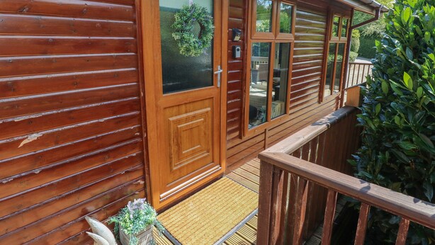 A wooden cabin with a balcony, large windows, and a door with a glass panel. - 1 Hornbeam Lodge (Narberth)