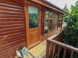 A wooden cabin with a balcony, large windows, and a door with a glass panel.