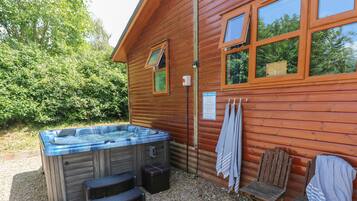A wooden cabin with a hot tub, outdoor seating, and a sign indicating spa rules.