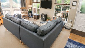 A living room with a sectional sofa, a wooden chair, a TV, and a fireplace. - 1 Hornbeam Lodge (Narberth)