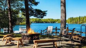A lakeside outdoor seating area with a fire pit, benches, and lounge chairs.
