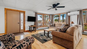 A spacious living room with a large window, a ceiling fan, and a flat-screen TV.