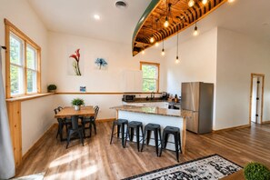 A modern kitchen with wooden flooring, a dining area with a table and chairs, and a bar counter with stools.