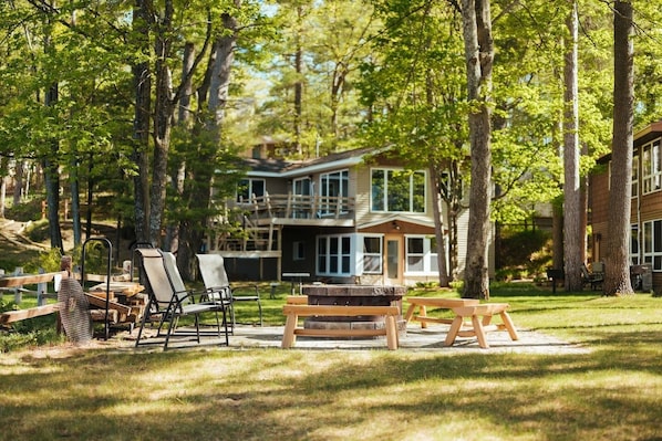 A cabin with a deck, outdoor seating, and a large window overlooking a forested area.